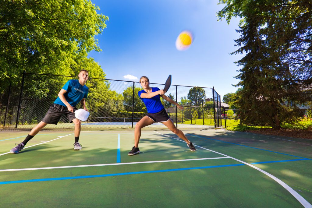 Caucasian young man and young woman pickleball player in action. They are holding pickleball paddles playing double, posing to return the ball in a pickleball court. Photographed in horizontal format with copy space.