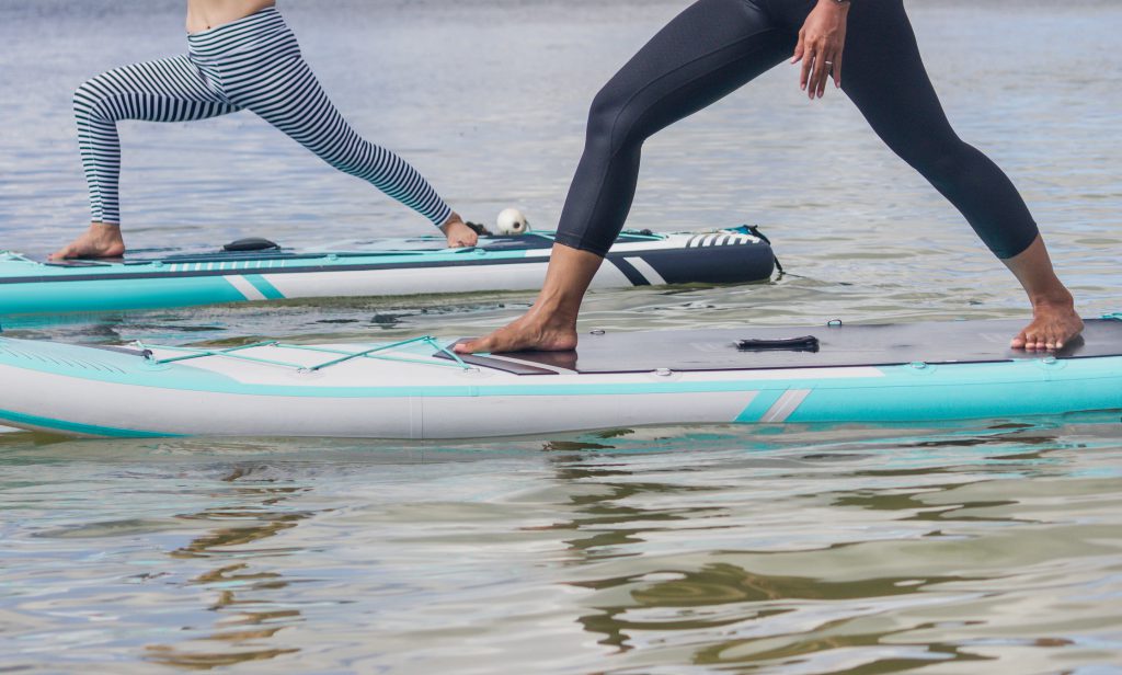 Cropped shot of two unrecognizable Asian senior woman doing a warrior yoga pose on top of a surf paddle board on the sea