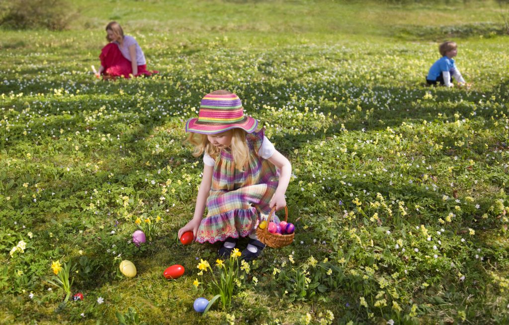 a little girl dressed up for Easter picking up eggs at the local egg hunt at a local park